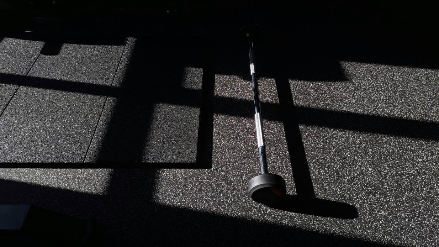 Barbell shadow across a dark gym floor